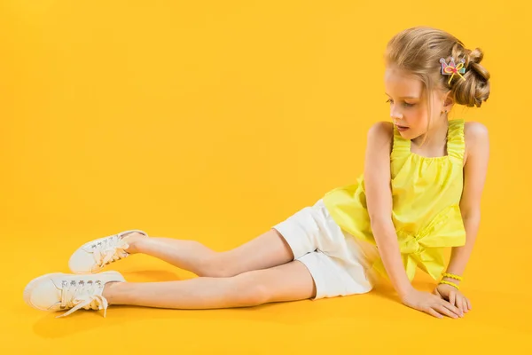 Ein Teenager-Mädchen sitzt auf gelbem Hintergrund. — Stockfoto