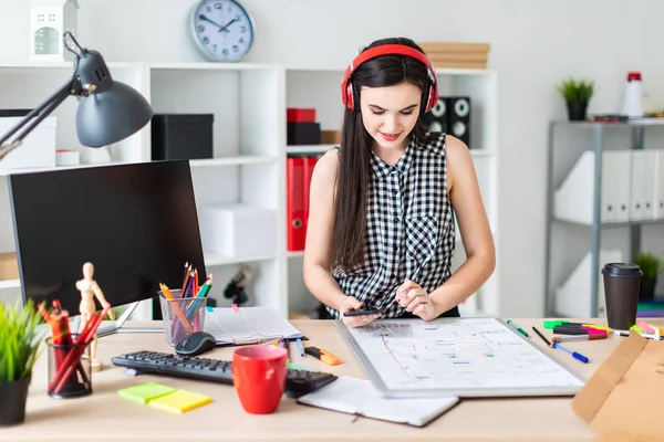 Genç bir kız bir tablo duruyor ve bir işaretleyici ve telefon elinde tutar. Bir manyetik tahta tablodur.