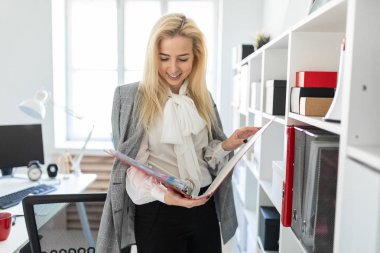 Ofis ve belgeler ile bir klasör üzerinden verilirse bir raf yakınındaki bir genç kız duruyor.
