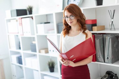 Güzel bir genç kız ofiste bir yığın yakınındaki anlamına gelir ve bir klasör belgeler ile onun elinde tutan.