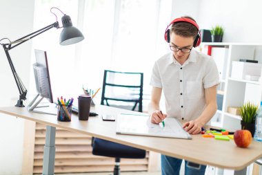 Gözlüklü ve kulaklıklı genç bir adam manyetik tahtaya bir işaret çizer..