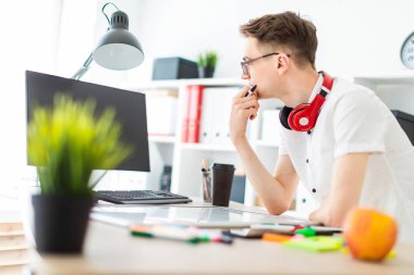 Gözlüklü genç bir adam bir bilgisayar masası duruyor. Genç bir adam bir bilgisayar ve bir manyetik kurulu ile çalışır. Çocuklar kulaklık boynuna asmak.