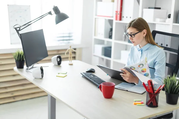 Una joven con gafas se sienta en una mesa en la oficina, sostiene un lápiz en la mano y trabaja con documentos . — Foto de Stock