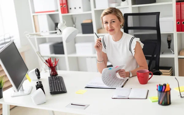 Een jong blond meisje zit achter een computerbureau in het kantoor, houdt een potlood in haar hand en werken met documenten. — Stockfoto