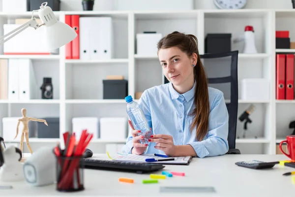 En ung flicka sitter vid ett bord på kontoret och innehar en vattenflaska i handen. — Stockfoto