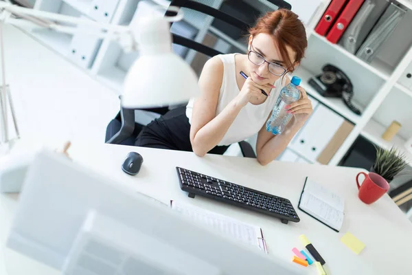 Красивая молодая девушка в офисе работает с документами, смотрит на монитор и держит бутылку воды . — стоковое фото