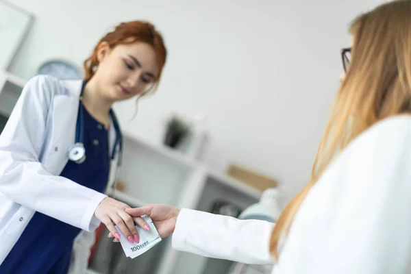 Una bella ragazza in una veste bianca è in piedi vicino a una scrivania del computer in ufficio e comunicare con l'interlocutore. L'interlocutore stringe la mano alle ragazze e le passa i soldi . — Foto Stock