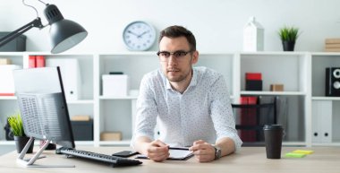 Gözlüklü genç bir adam ofiste bir tabloda yakınındaki standları ve elinde bir kalem tutar.