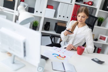 Genç bir kız telefonda ofis ve çekici fotoğraf masada oturuyor.