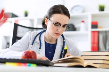 Beyaz bir elbise içinde güzel bir genç kız bir marker ve bir kitap ile bilgisayar masasında oturuyor. Netlik, kız vurgulanan bir odak derinliği olan bir fotoğraf.