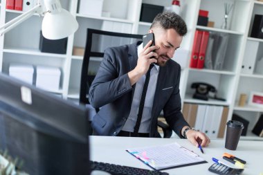 Bir adam masada, ofisinde oturuyor telefonda konuşurken ve belgeleriyle çalışma.