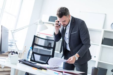 Bir adam ofiste bir tabloda yakın duran, telefonda konuşurken ve belgeler üzerinden çevirme.