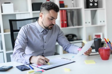 Ofiste genç bir adam bir masada oturuyor, bir işaretleyici elinde tutuyor ve belgeleriyle çalışır.
