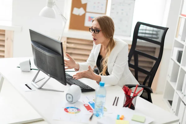 Een jong meisje is zittend aan een tafel in het kantoor, kijken naar de monitor en benieuwd wat er gebeurd is. — Stockfoto