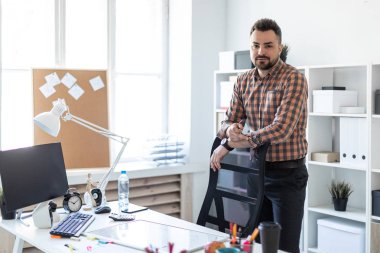 Bir adam bilgisayar masası yakınındaki ofiste standları ve sandalyenin arkasında ellerini koyar.