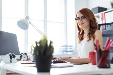 Güzel genç kız ofiste masada oturan ve klavyede yazarak.