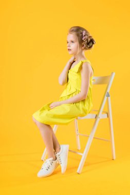 Bir kız sarı bir arka plan üzerinde beyaz bir sandalyede oturuyor.