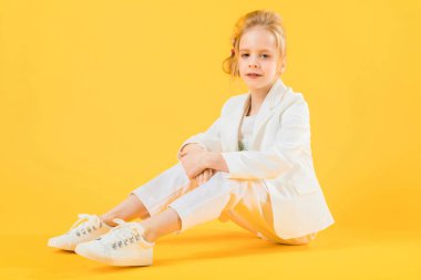 Beyaz giysili bir genç kız bacaklarını ileri sarı bir arka plan üzerinde uzanan oturur.