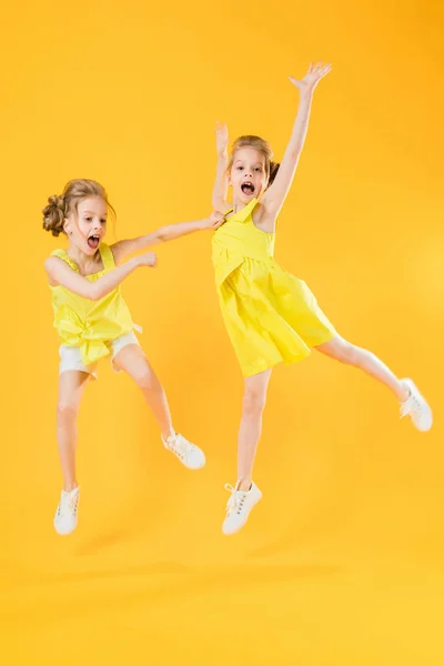Holky dvojčata spolu tančí na žlutém podkladu. — Stock fotografie