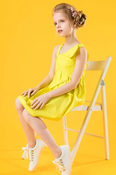 Ένα κορίτσι κάθεται σε μια λευκή καρέκλα σε κίτρινο φόντο. — Φωτογραφία Αρχείου