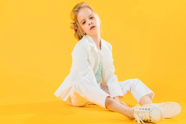 Ein junges Mädchen in weißen Kleidern sitzt und streckt ihre Beine vor einem gelben Hintergrund. — Stockfoto