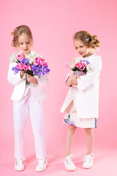 Gemelas en ropa ligera con ramos de flores de pie sobre un fondo rosa . — Foto de Stock