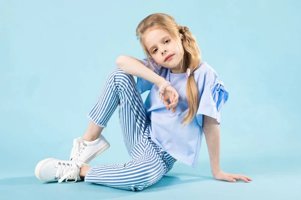 A girl in blue clothes is sitting on a blue background. — Stock Photo, Image
