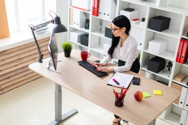 Genç bir kız masanın ayakta ve metin klavyede yazarak. Belgeler ve bir işaretleyici kızın yanında yalan.