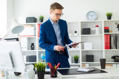 Genç bir adam ofiste bir tabloda yakınındaki duruyor ve bir kalem ve belgeleri tutar.