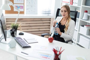 Genç bir kız ofiste bir masada oturur ve elinde bir şişe su tutar. Önce kız masanın üzerinde bir elma.