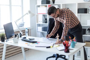 Bir adam ofiste masanın yanında duruyor ve bir işaretleyici manyetik tahtaya çizer.
