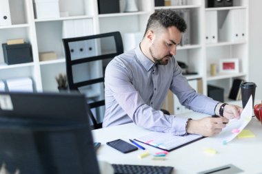 Ofiste genç bir adam bir masada oturuyor, bir işaretleyici elinde tutuyor ve belgeleriyle çalışır.