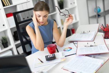 Genç bir kız onun ofisinde bir masada oturur ve gözlük onun elinde tutan.