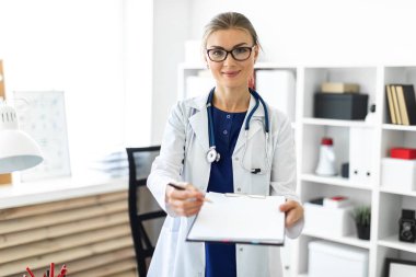 Bir genç kız Beyaz paltolu bir tablo ofisinde yakınındaki duran ve bir tablet ve kalem tutan. Bir stetoskop boynunda asılı.