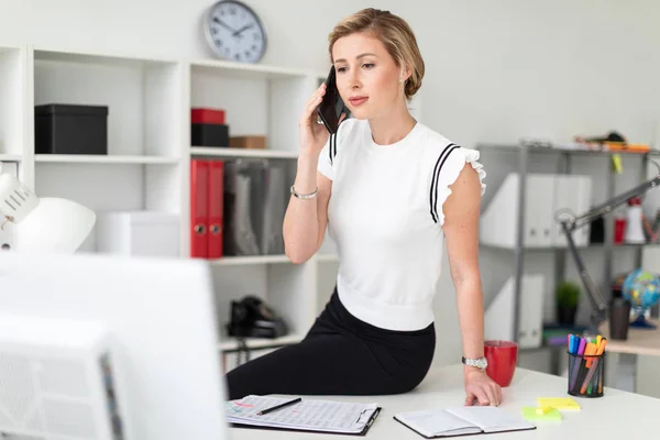 Une jeune fille blonde est assise au bureau et parle au téléphone . — Photo