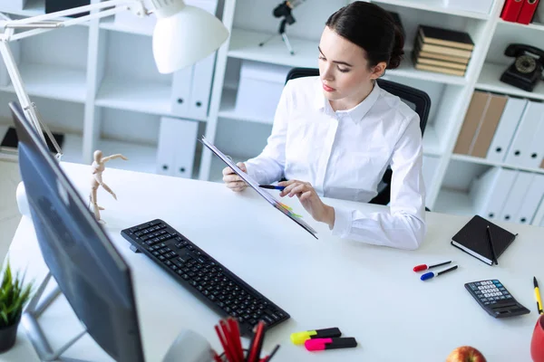 Молодая девушка в офисе держит ручку в руке и работает с документами и компьютером . — стоковое фото