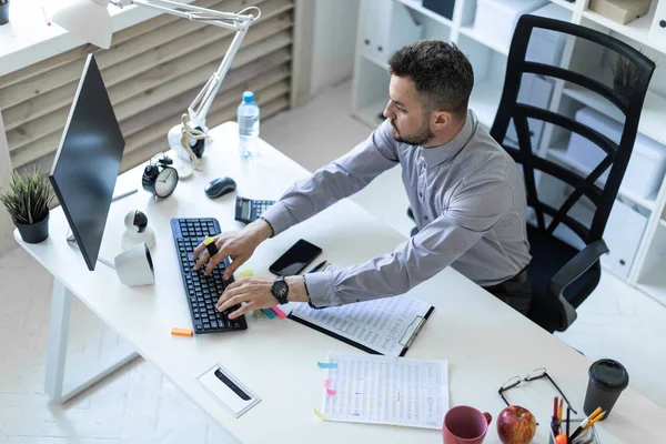 Молодой человек в офисе сидит за столом, держит маркер в руке и работает с документами и компьютером . — стоковое фото
