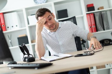 Genç bir adam ofiste bir masada oturur ve elini başına tutar.