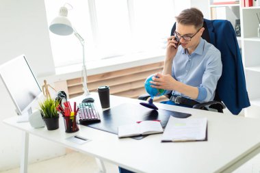 Genç bir adam telefonda konuşurken ve globe adlı arıyorsunuz bir bilgisayar masası ofisinde oturuyor.