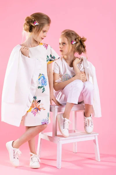 Dvojčata holky ve světlé oblečení pózuje u schodiště se dvěma kroky na růžovém pozadí. — Stock fotografie