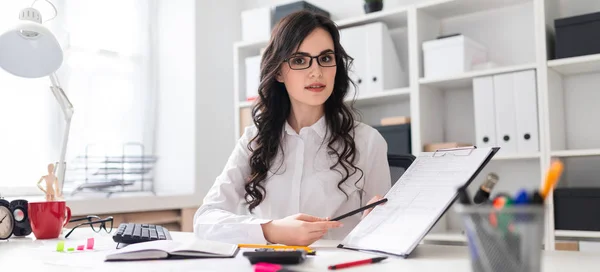 Een mooi jong meisje is zittend aan een tafel in het kantoor en een potlood wijzend op de informatie in het document. — Stockfoto