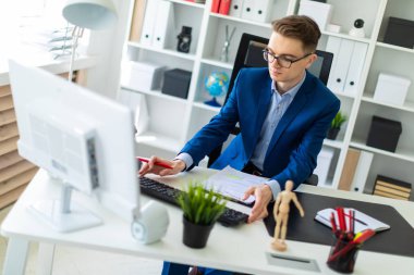 Belgeler ve bir bilgisayar ile ofis ve çalışan bir masada genç bir adam oturuyor.