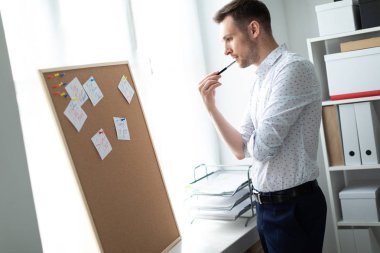 Genç adam çıkartmaları ile yakındaki tahta ayakta ve bir kalem dudaklarına büyüdü.