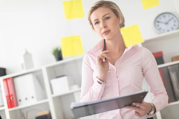 Una joven rubia se para en la oficina junto a un tablero transparente con pegatinas y sostiene documentos y un lápiz en sus manos. — Foto de Stock