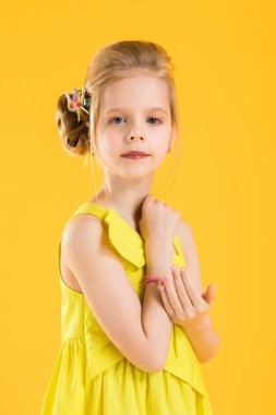 Bir kız sarı bir arka plan üzerinde beyaz bir sandalyede oturuyor.