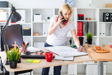 Genç bir kız bir masanın ayakta, telefonda konuşurken ve bir işaretleyici elinde tutan. Masaya manyetik bir pansiyondur. Kızlar kulaklık boynuna asmak.