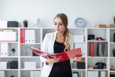 Genç bir kız ofis raf yanında duruyor ve bir klasör belgeler ile onun elinde tutan.