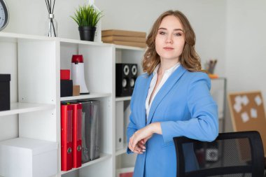 Güzel bir genç kız ofiste, bir raf yakınındaki bir dirsek bir sandalyenin arkasına koyarak standları.