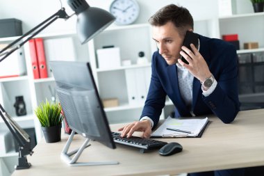 Genç bir adam ofiste bir tabloda yakın duran, telefonda konuşurken ve metin klavyede yazma.