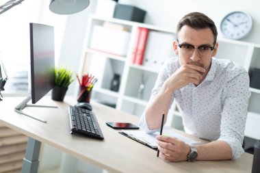 Gözlüklü genç bir adam ofiste bir tabloda yakınındaki duruyor ve bir kalem elinde tutuyor.